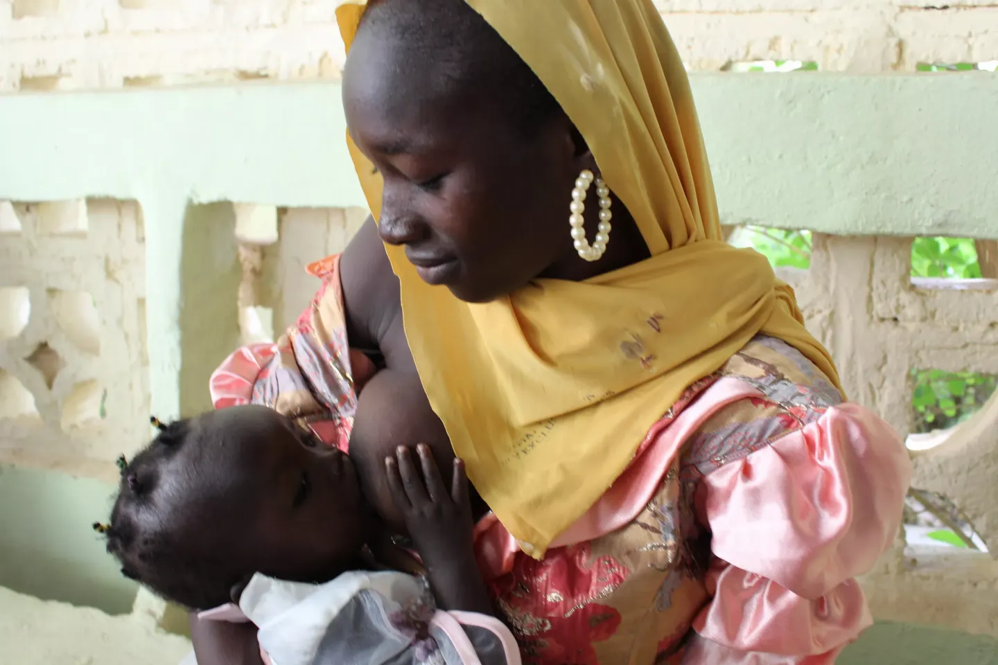 A mother wearing a yellow headscarf breastfeeds her baby